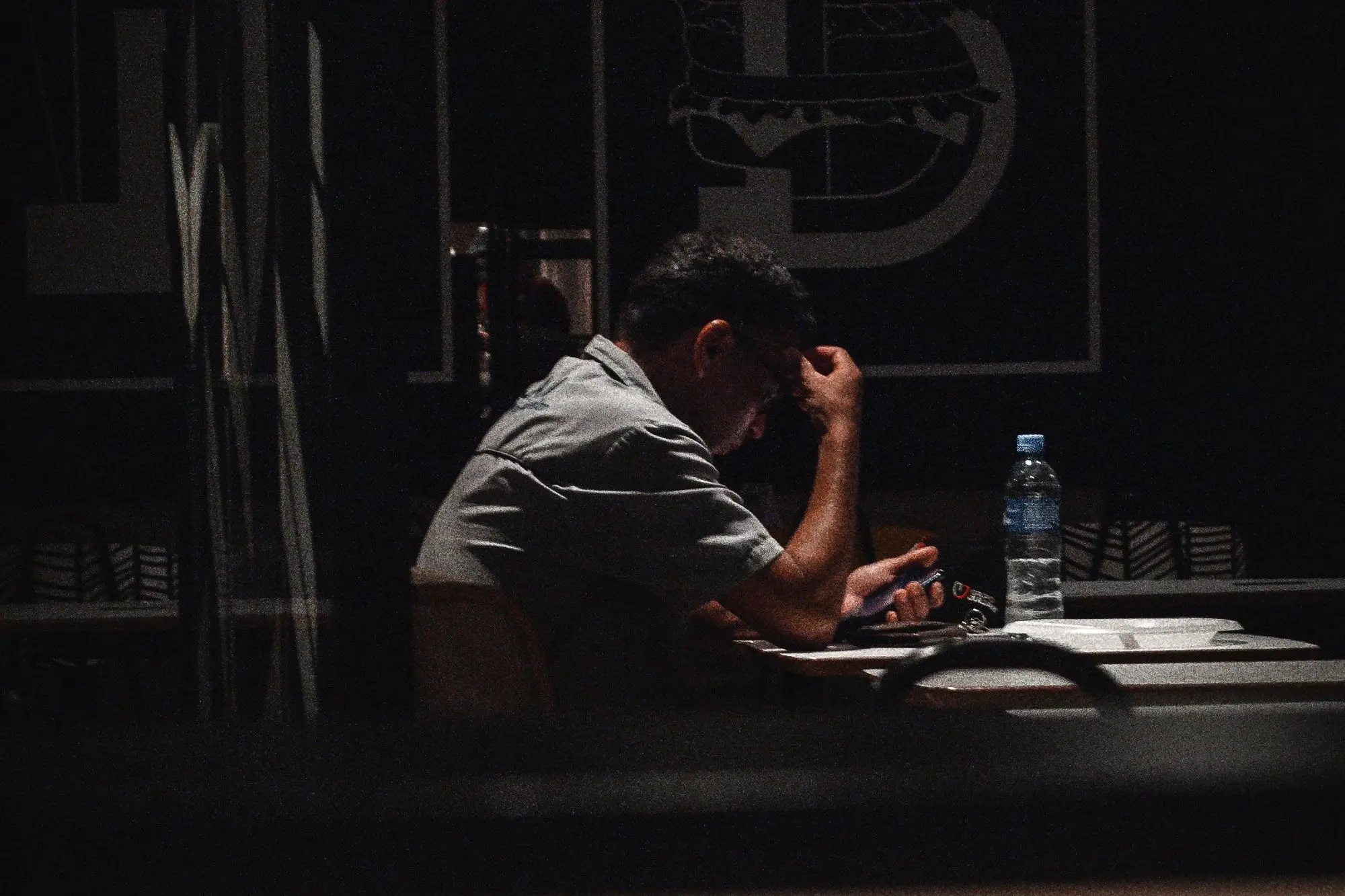 Burger shop owner sitting alone after closing, head in hand, reading a payment alert on his phone